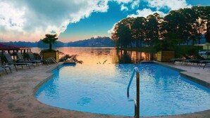 Una piscina con sillas de descanso y vistas al lago al atardecer.