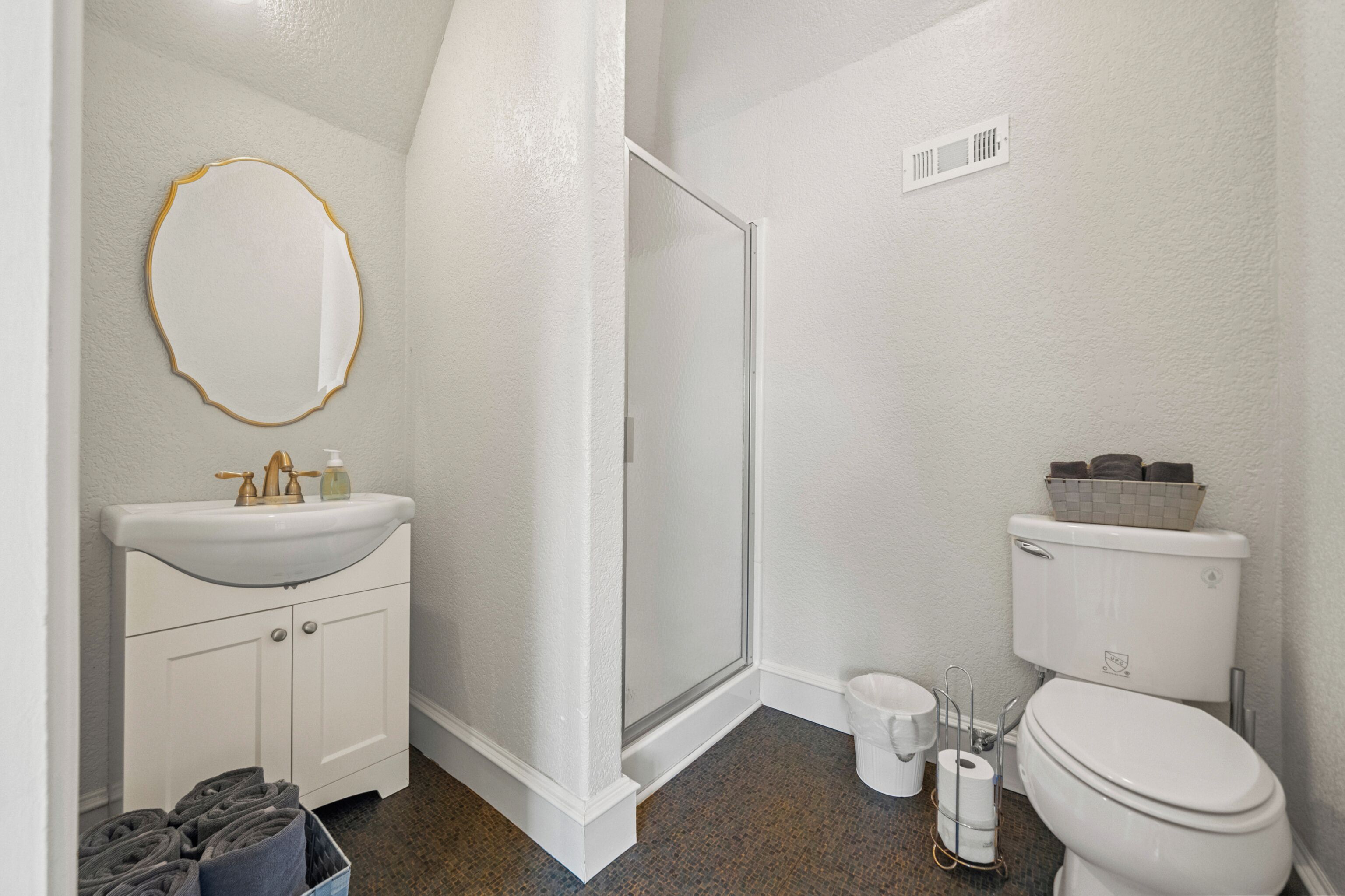 A bathroom with a white sink, a mirror, a shower, and a toilet.