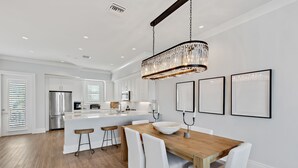 Una cocina moderna con armarios blancos, una mesa de comedor de madera y una lámpara de araña colgante.