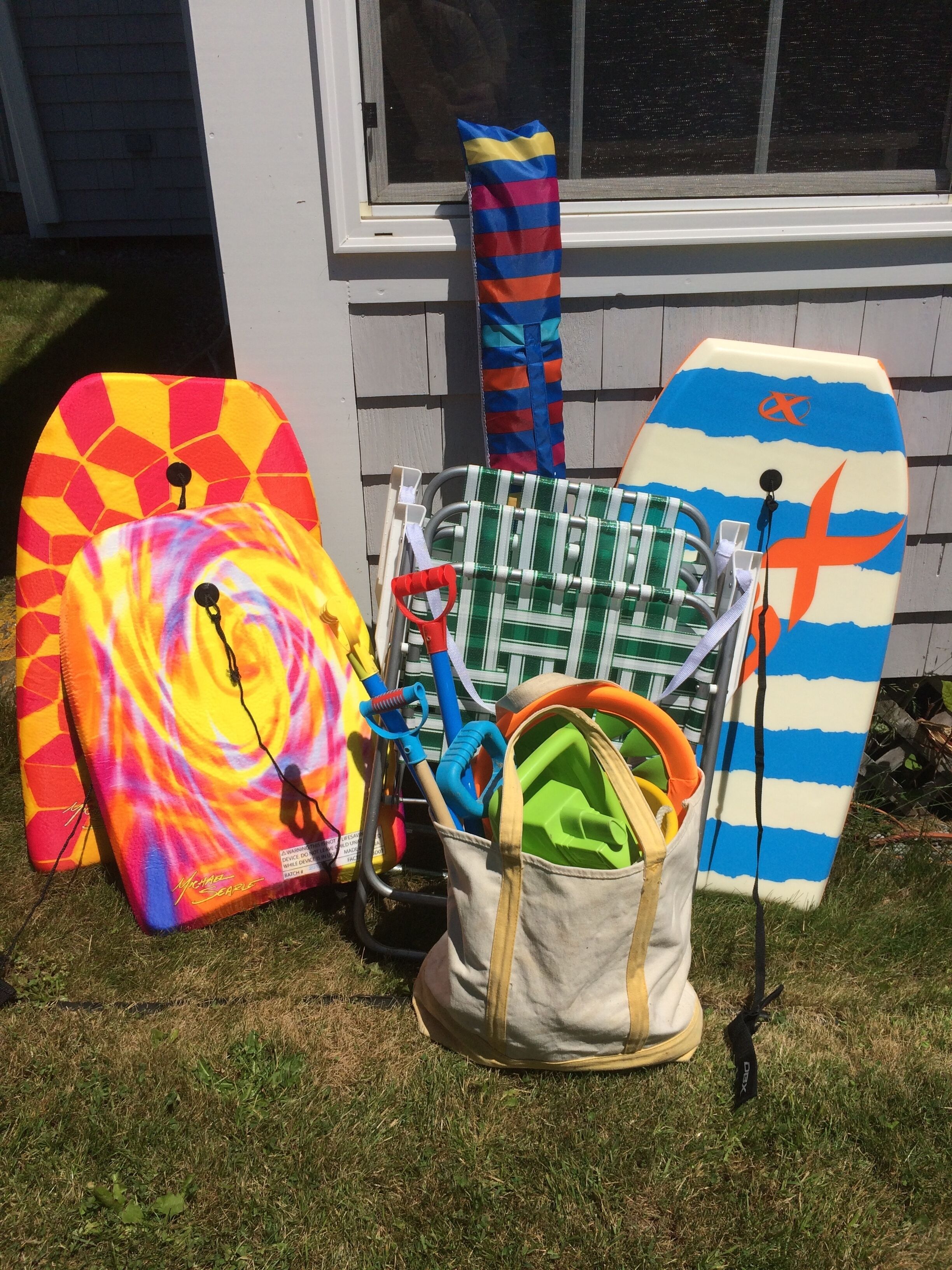 A collection of colorful surfboards and a bag of cleaning tools on a grassy lawn in front of a house.