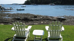Due poltrone Adirondack bianche rivolte verso una costa rocciosa con barche in acqua.