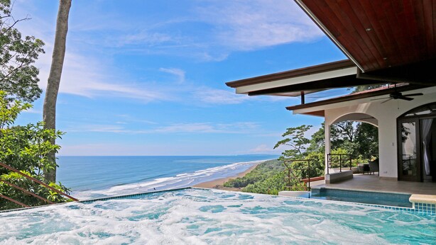 Un jacuzzi con vista al océano, una pérgola de madera y un patio cubierto.