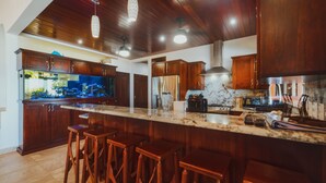 Una cocina moderna con armarios de madera, una isla grande con taburetes de bar, un acuario y una campana extractora de acero inoxidable.