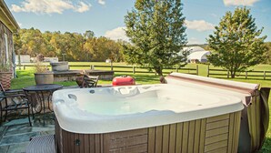 Un jacuzzi en un patio trasero con terraza de madera, sillas y una parrilla.