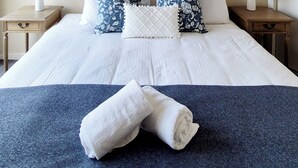 Un lit bien fait, agrémenté d’oreillers blancs et bleus à motifs, d’un plaid bleu et de deux tables de chevet avec des lampes.