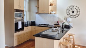 Une cuisine moderne avec des meubles en bois, un îlot central doté de tabourets, un four à micro-ondes, un four traditionnel et une grande horloge murale.