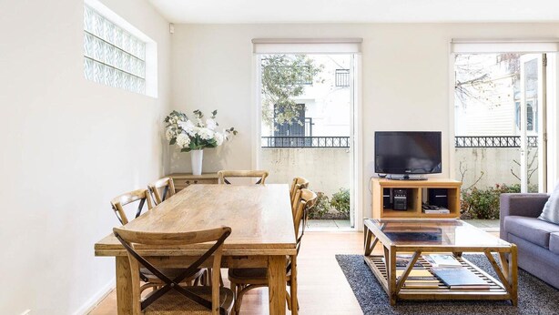 Un salon spacieux avec une table à manger en bois, un canapé et un téléviseur posé sur un meuble en bois.