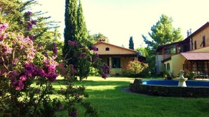 Una propiedad residencial con césped cuidado, una fuente y árboles maduros.