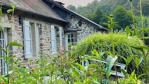 A stone building with a sloped roof and a chimney, surrounded by lush greenery and a clear sky. - Le Gite De Parc (2 Bedrooms, Sleeps 4) (Souleuvre En Bocage)
