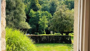 A view through an open doorway to a lush garden with a pathway leading to a white bench. - Le Gite De Parc (2 Bedrooms, Sleeps 4) (Souleuvre En Bocage)