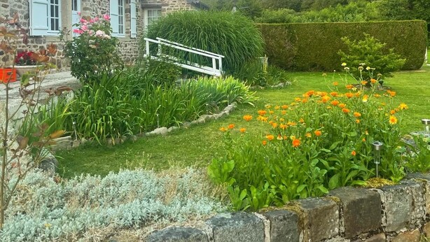 A stone house with a white fence, a garden with various plants and flowers, and a clear sky. - Le Gite De Parc (2 Bedrooms, Sleeps 4) (Souleuvre En Bocage)