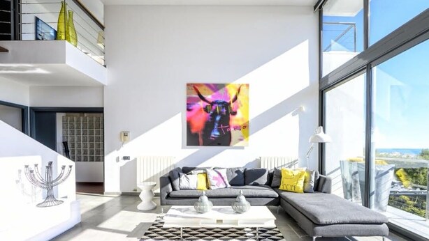 Un salon moderne avec un canapé d’angle gris, une table basse blanche et un tableau abstrait aux couleurs vives accroché au mur.