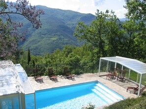 Piscina con vistas a montañas, rodeada de sillones de descanso y una zona de estar cubierta.
