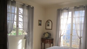 Une chambre à coucher avec un lit, une commode, un miroir et une fenêtre avec des rideaux.