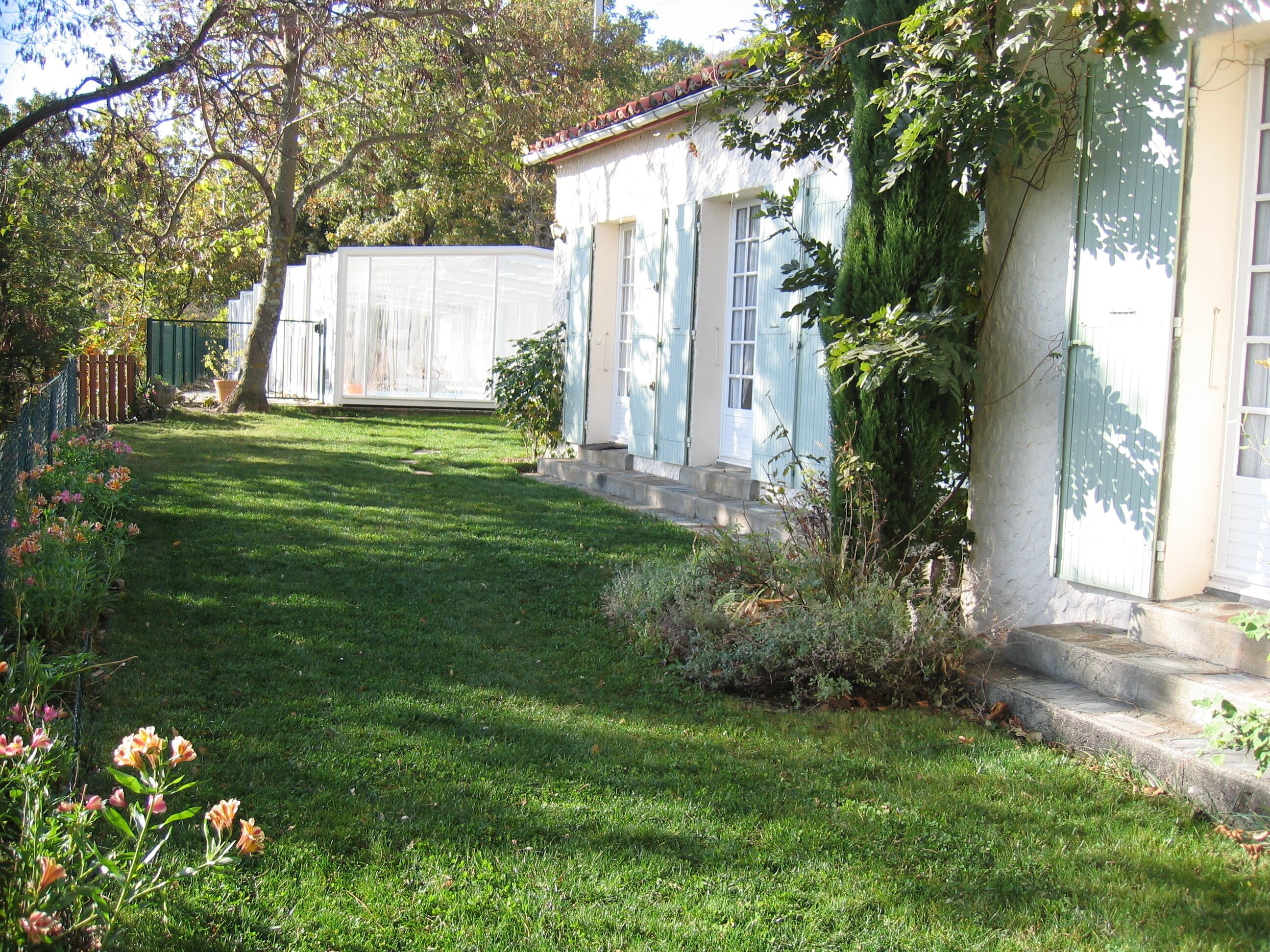 Un giardino curato con prato, piante fiorite e un edificio bianco con persiane blu.