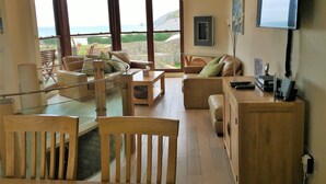 Een ruime woonkamer met een groot raam met uitzicht op zee, een houten eettafel en een comfortabele zithoek.