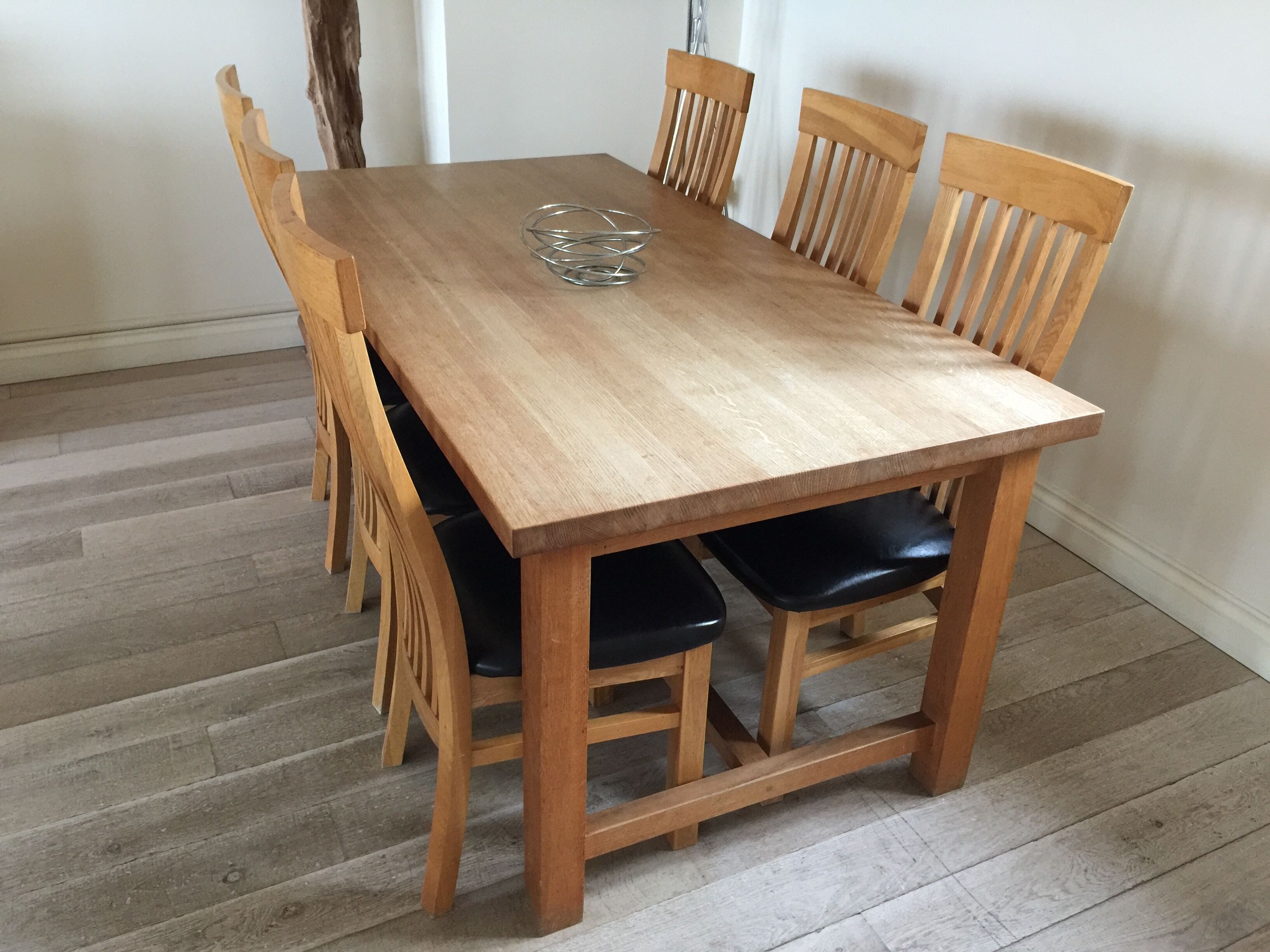 Une table à manger en bois, avec six chaises, un verre posé sur la table et un plancher en bois.