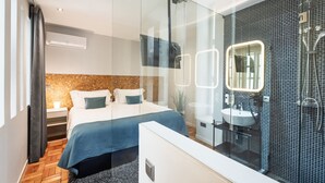 Un dormitorio moderno con una cama grande, mesitas de noche, un separador de vidrio, un baño con lavamanos y espejo, y una zona de ducha.