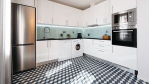 Una cocina moderna con armarios blancos, un refrigerador de acero inoxidable, una lavadora y un microondas.