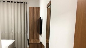Quarto de hotel com chão de madeira, cama com roupa de cama branca, guarda-roupa de madeira, televisão de tela plana na parede e puxador de porta moderno.
