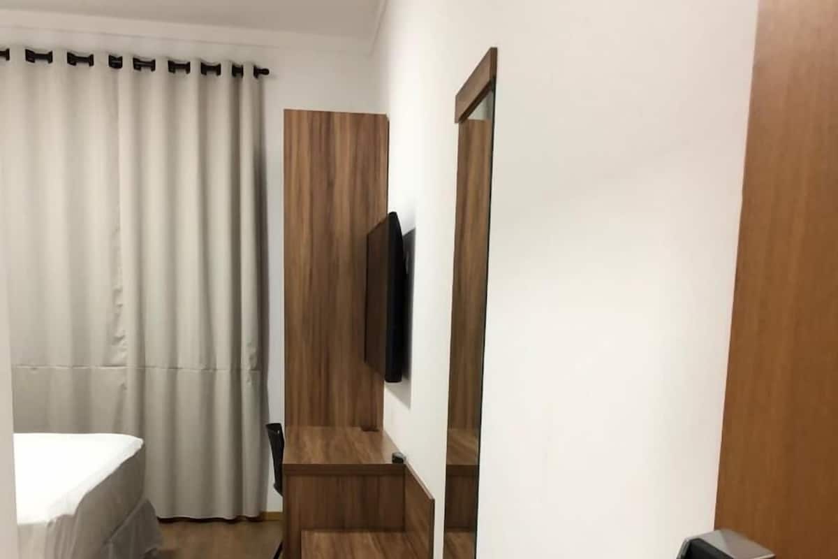 A hotel room with a wooden floor, a bed with white bedding, a wooden wardrobe, a flat-screen TV mounted on the wall, and a modern door handle.