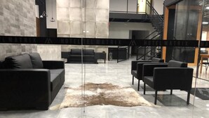 Um hall de hotel moderno com sofá de couro, poltronas e divisória de vidro.