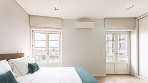 A bedroom with a bed, a window, an air conditioning unit, and a view of buildings outside. - Feel Porto Downtown City Roofs (Oporto)