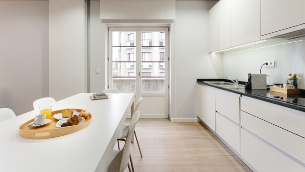 A modern kitchen with a breakfast tray on a white table, a window with a view of buildings, and white cabinetry. - Feel Porto Downtown City Roofs (Oporto)