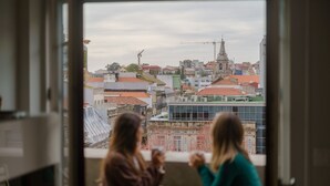 Two women sitting at a table by a window overlooking a cityscape with buildings and a church. - Feel Porto Downtown City Roofs (Oporto)
