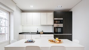 A modern kitchen with white cabinets, a black countertop, and a dining area with a white table and chairs. - Feel Porto Downtown City Roofs (Oporto)