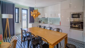 Una cocina moderna con armarios blancos, una mesa de comedor de madera, sillas negras, una lámpara colgante y un microondas.