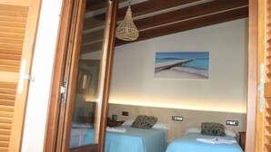 Een kamer met twee bedden, een houten plafond, een hanglamp en een schilderij van een strand.