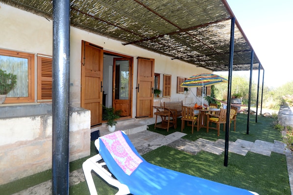 Un espace extérieur abrité, avec une table et des chaises, un fauteuil bleu et un parasol à rayures.