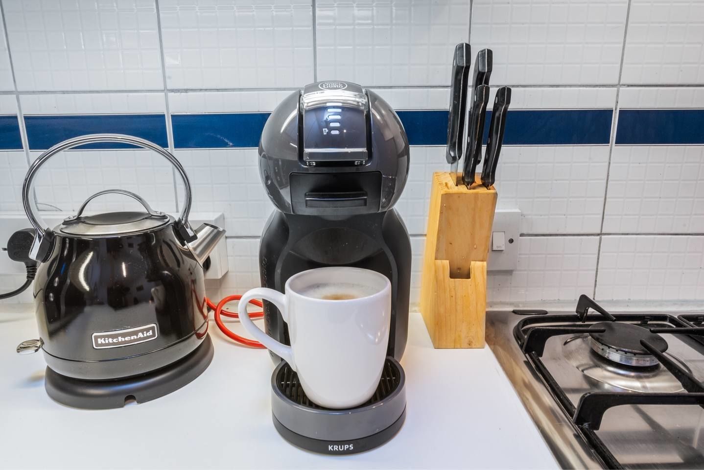 A coffee maker, a kettle, and a cup of coffee on a kitchen counter.