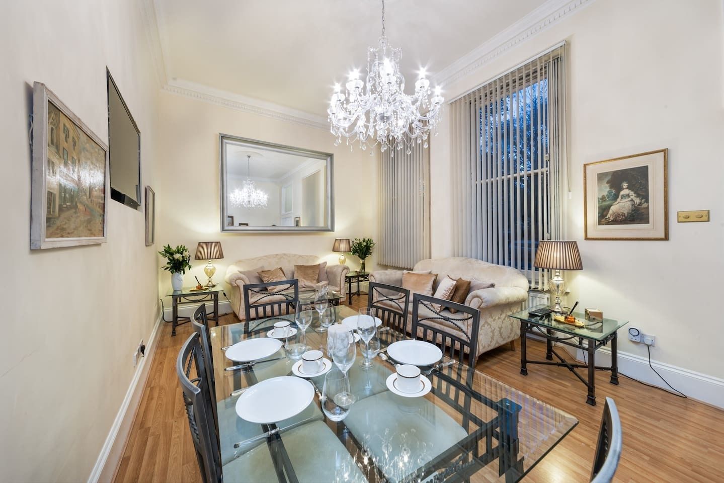 A dining area with a glass table set for four, a sofa, and a chandelier.