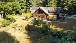 Una baita rustica con tetto spiovente, circondata da un giardino recintato e da una fitta foresta.