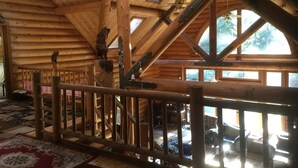 Interno di una baita in legno con una scala in legno, una ringhiera in legno e vista all'esterno attraverso ampie finestre.