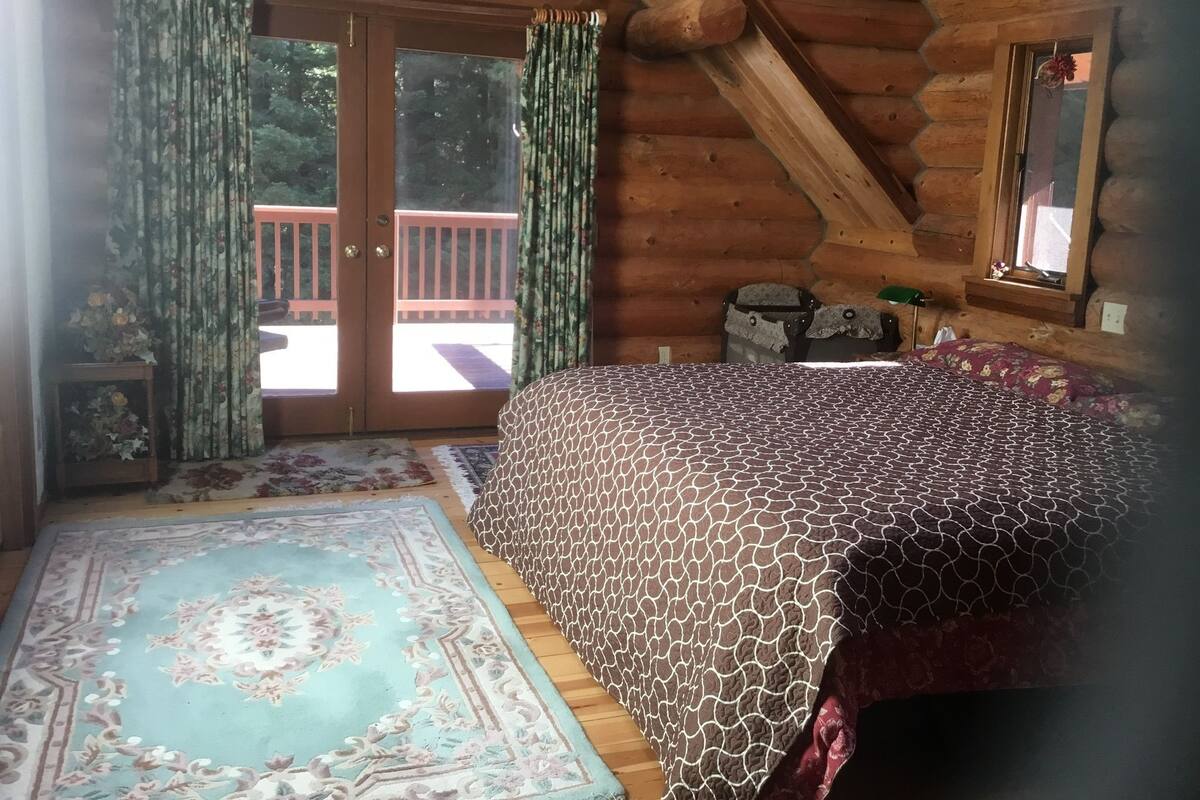 A log cabin bedroom with a bed, a rug, and a window with curtains.