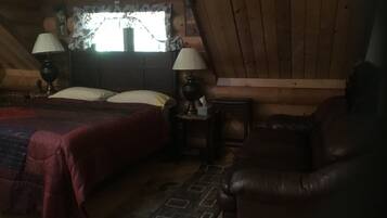 A cozy attic bedroom with a bed, two bedside lamps, a leather armchair, and a window with floral curtains.