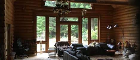 A log cabin interior with a large window, a sofa, a chair, and a rug.