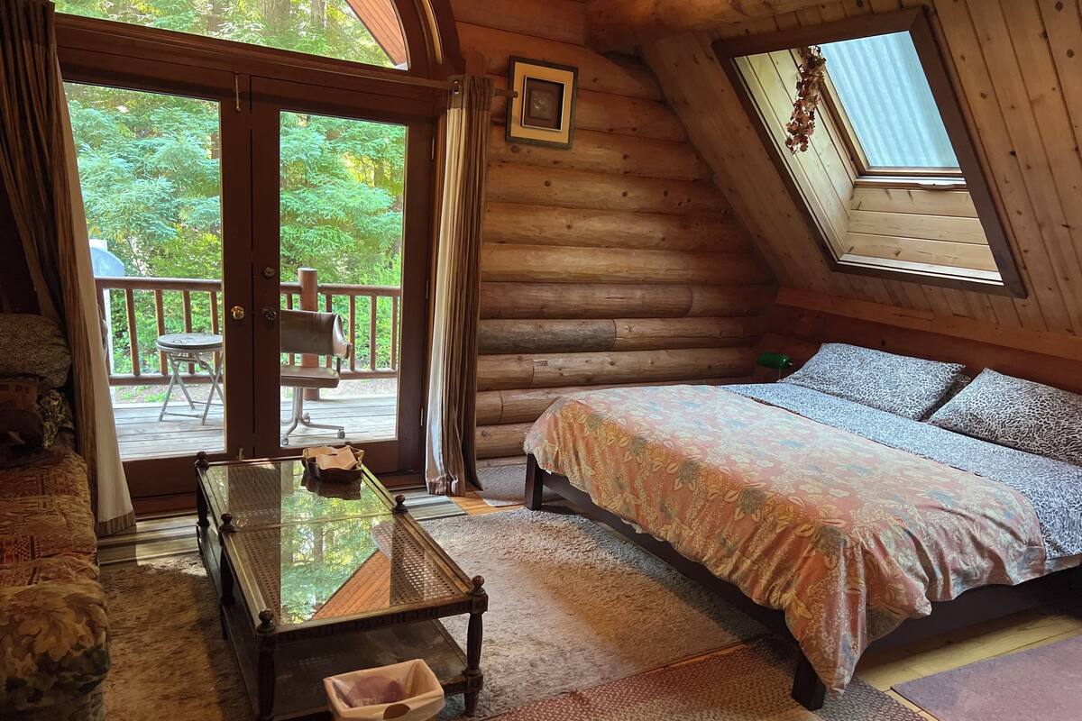 A log cabin bedroom with a bed, a table, and a chair.