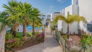 A pathway leading to a pool surrounded by palm trees and a white building. - Beautiful contemporary Villa (Orihuela)