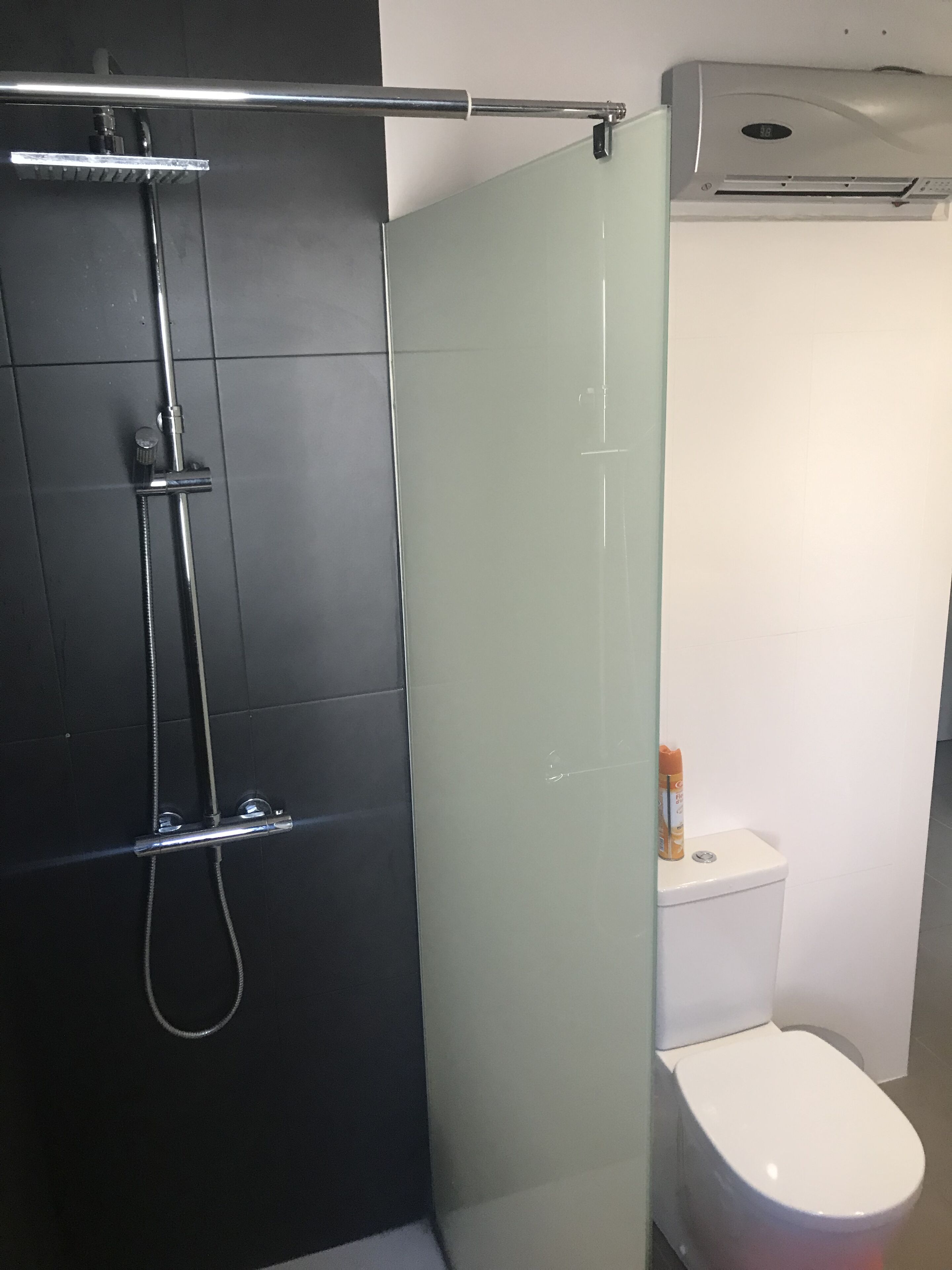 A modern bathroom with a glass shower enclosure, a white toilet, and a wall-mounted air conditioning unit.