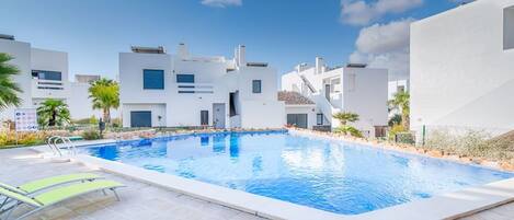 Un área de piscina moderna con piscina azul cristalina, piso de baldosas y algunas sillas de descanso.