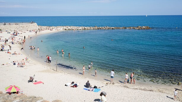 Een strand met helderblauw water, mensen die zonnebaden en een rotsachtige zeebaan.