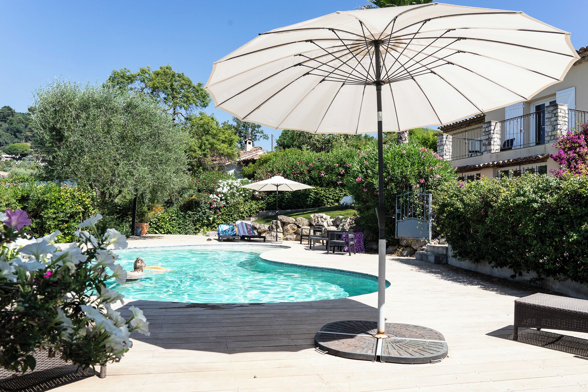 Un espace piscine doté d’un grand parasol, de chaises longues et d’une terrasse en bois.