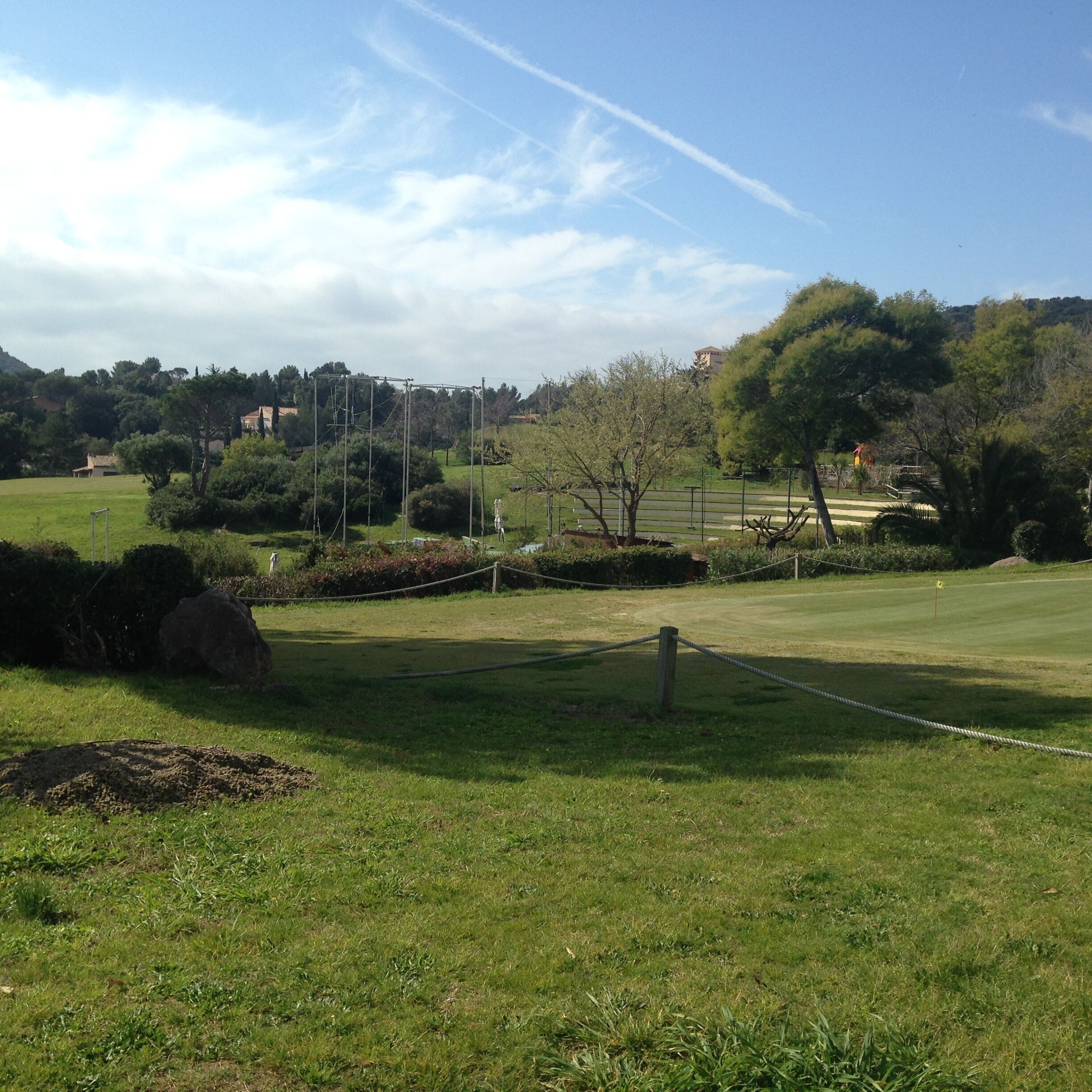 Un campo de golf con cielo despejado, árboles y edificios al fondo.