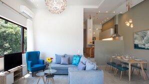 Ein modernes Wohnzimmer mit einem blauen Sofa, einem Fernseher und einem Essbereich mit Tisch für vier Personen.