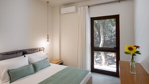 Ein Schlafzimmer mit einem Bett, einem Nachttisch, einer Vase mit Blumen und einem Fenster mit Blick auf Bäume.