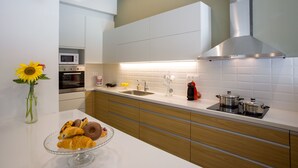 Eine moderne Küche mit weißen Schränken, einer Edelstahl-Dunstesse, einer Mikrowelle und einem Spülbecken. Auf der Arbeitsfläche steht eine Schüssel mit Gebäck.